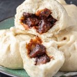 A plate of vegan char siu bao buns with one split open to reveal the char siu seitan inside