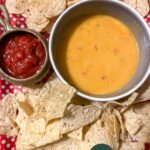 vegan queso in a bowl beside salsa, surrounded by tortilla chips